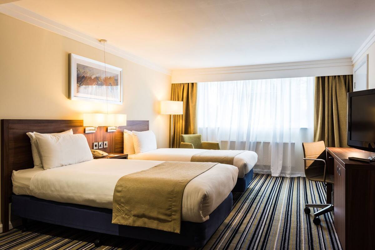 Habitación de hotel con dos camas, un escritorio, un televisor y una ventana con cortinas.