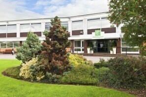 A building with a modern design, a well-maintained lawn, and a variety of trees. - Holiday Inn Chester - South (Chester)
