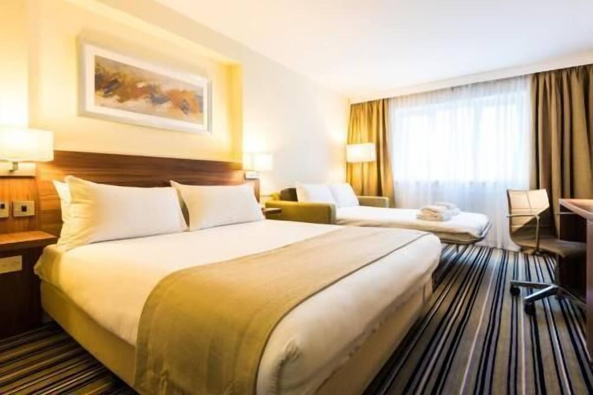 Una habitación de hotel con dos camas, un escritorio, una silla y un cuadro en la pared.
