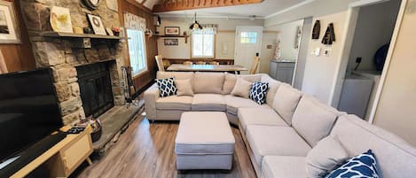 A living room with a stone fireplace, a large L-shaped sofa, and a wooden staircase.