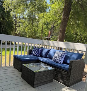 An outdoor seating area with a wicker sofa and a glass-top coffee table, surrounded by a white deck and lush greenery. - Newly Renovated 3 Bedroom House in Lakewood! (Durham)
