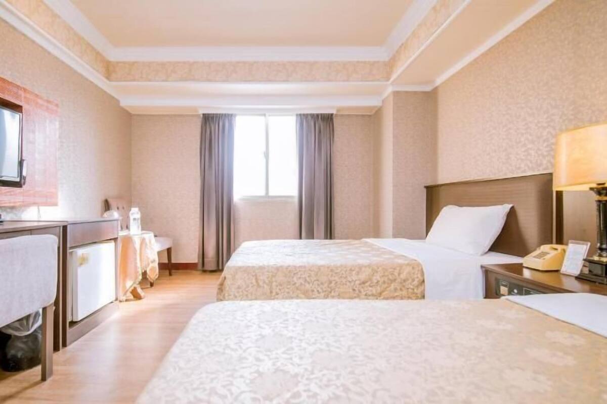 A hotel room with two beds, a desk with a TV, a lamp, and a telephone.