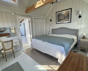 A bedroom with a bed, bedside tables, a desk, a chair, and a painting on the wall. - Bluebird Limit 4 2 Bedroom Cottage (Sebago)