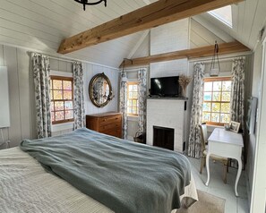 A bedroom with a bed, a dresser, a television, a fireplace, and a desk. - Bluebird Limit 4 2 Bedroom Cottage (Sebago)