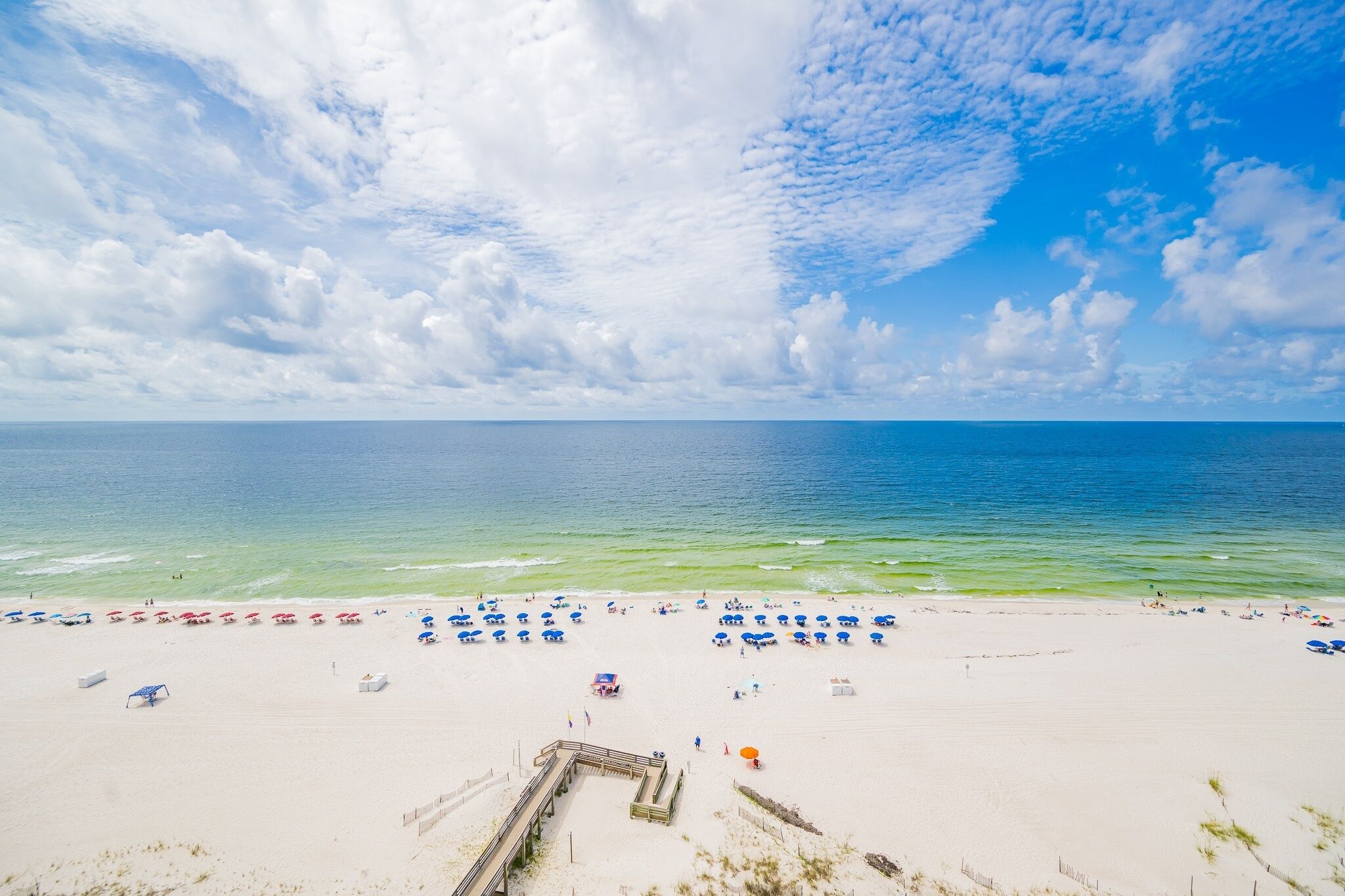 A beach with a wooden pier, clear blue sky, and calm sea.
