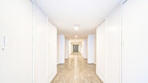 A long, narrow hallway with white walls and wooden flooring, leading to a door at the end. - Deluxe Super Townhouse Lakdikapul (Hyderabad)