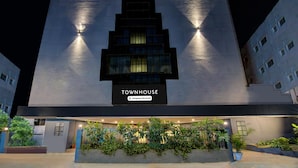 A modern building with a sign reading "TOWNHOUSE" and "Company-Serviced." It features a prominent entrance with a well-lit facade and a landscaped area with plants. - Deluxe Super Townhouse Lakdikapul (Hyderabad)