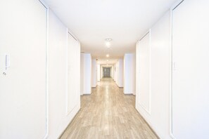 Un long couloir étroit aux murs blancs et au plancher en bois, qui mène à une porte au fond.