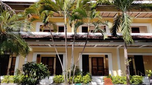 Un edificio de varios pisos con piscina, palmeras y una tumbona de madera.