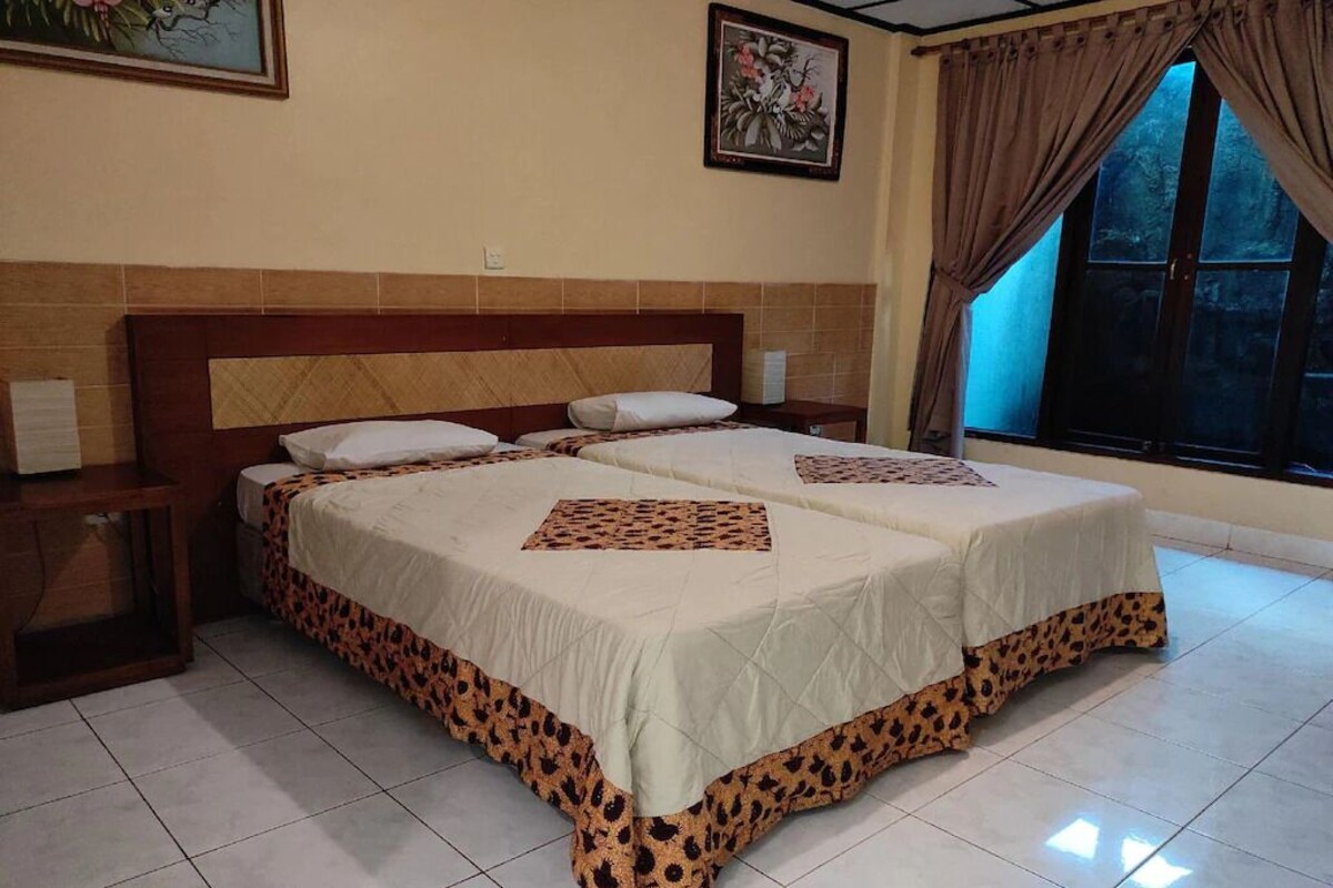 Una cama doble con edredón estampado de leopardo, cabecera de madera, mesita de noche con lámpara y ventana con cortinas.