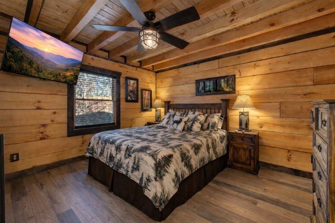 A wooden cabin bedroom with a bed, a ceiling fan, a window, and a nightstand.