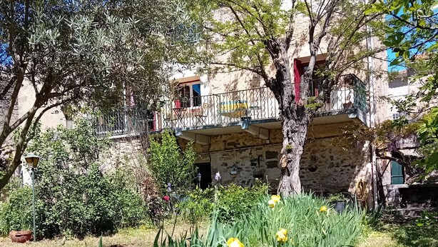 Ein Steinhaus mit Balkonen, umgeben von Grünpflanzen und Blumen.