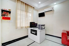 A reception desk labeled 'TOWNHOUSE Company Service,' a flat-screen TV, an air conditioning unit, a red chair, and a window with curtains. - Deluxenirmala Palace (Jodhpur)