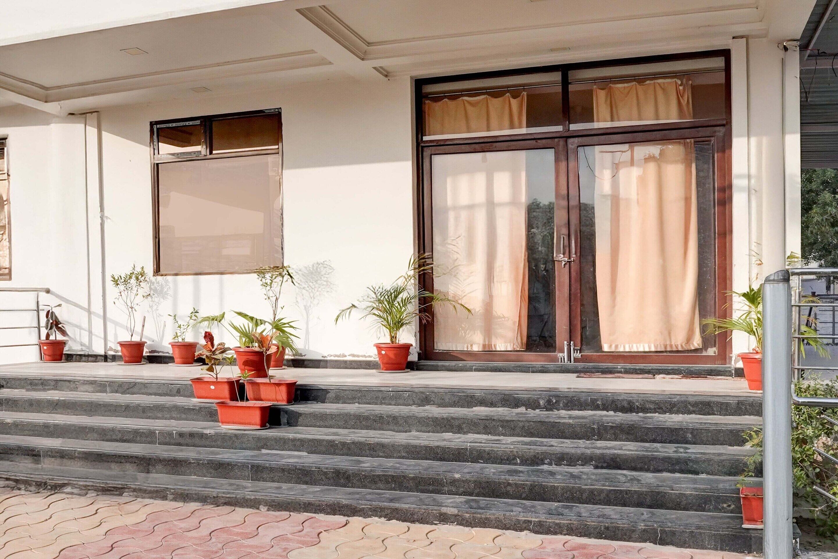 A building entrance with steps, potted plants, and a large glass door with curtains.