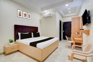A modern bedroom with a wooden bed, bedside tables, a TV, and a small seating area.