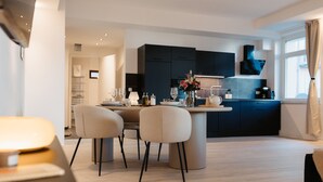 A modern kitchen with dark cabinets, a dining area with a round table and chairs, and a window with curtains.