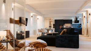 A modern living room with a dark sofa, wooden chairs, and a dining area with a table and chairs.