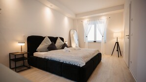 A bedroom with a bed, bedside lamps, a mirror, a window with curtains, and a tripod lamp.
