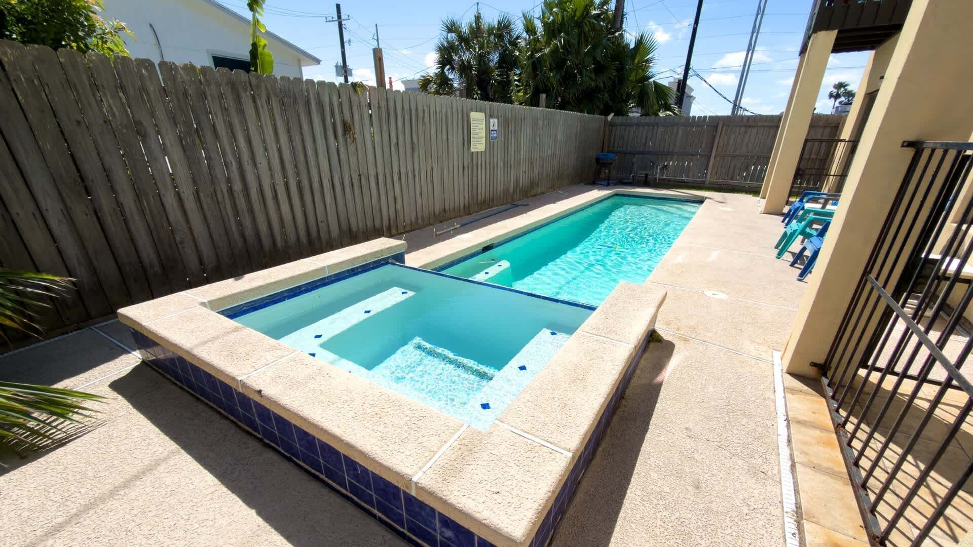 Une piscine extérieure rectangulaire, dotée d’une plage carrelée, entourée d’une clôture en bois et agrémentée d’un portail en métal.