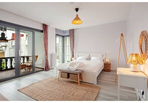 A bedroom with a bed, a bedside table, a lamp, a bench, a window, and a balcony.