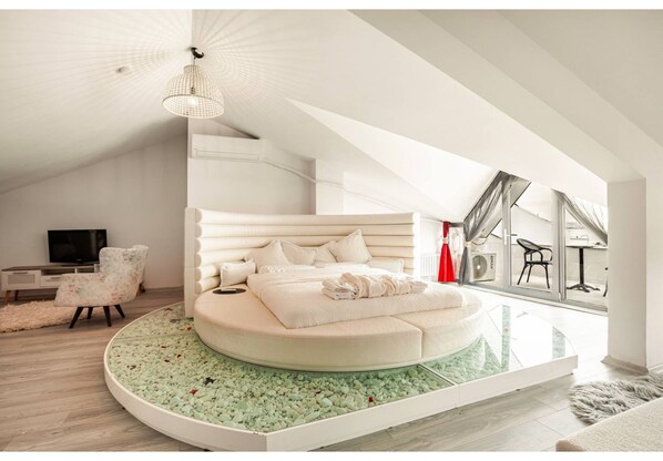 A modern bedroom with a circular bed, a television, a chair, and a large window.