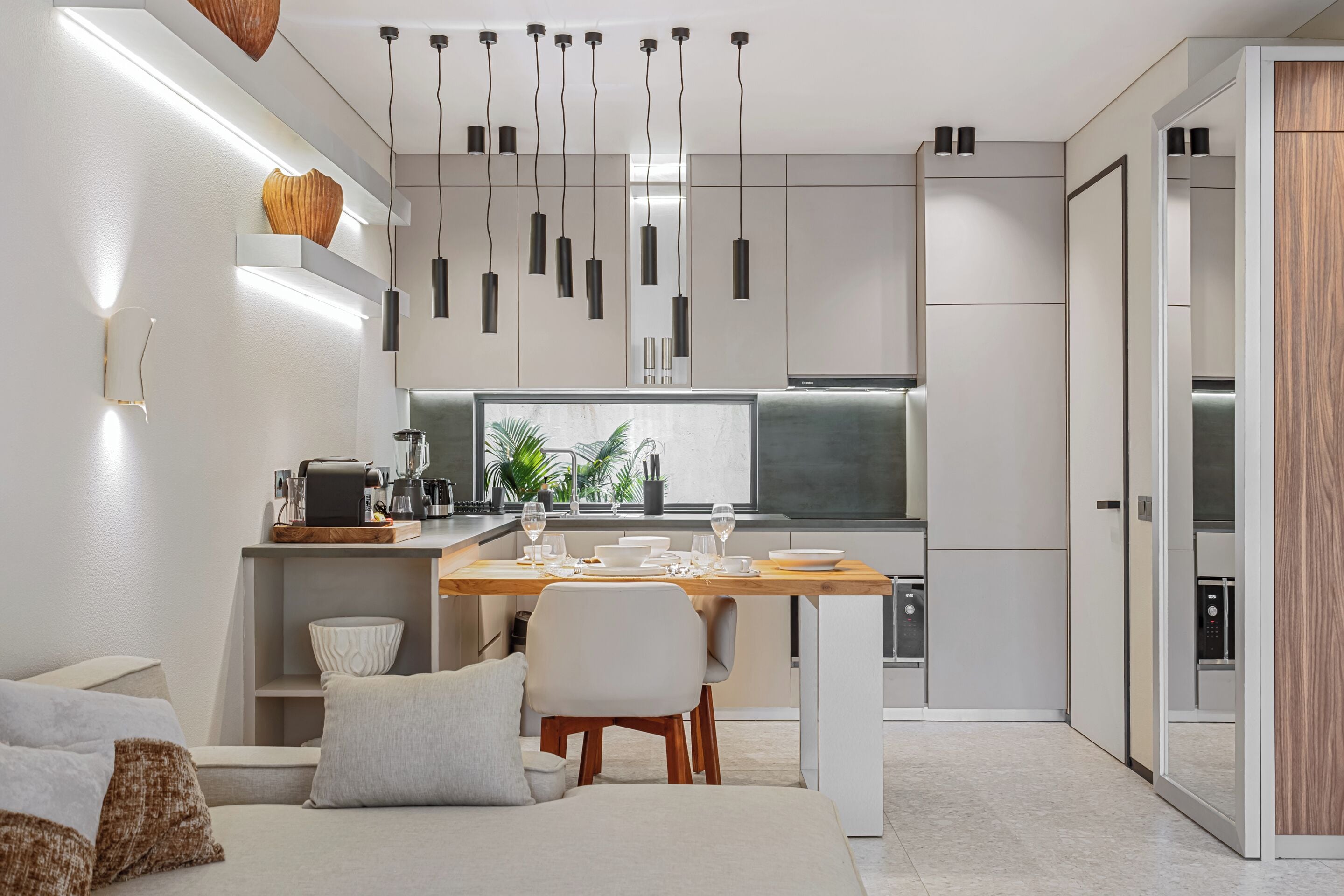 Une cuisine moderne avec un coin repas, des meubles blancs, un éclairage suspendu et une cuisinière intégrée.