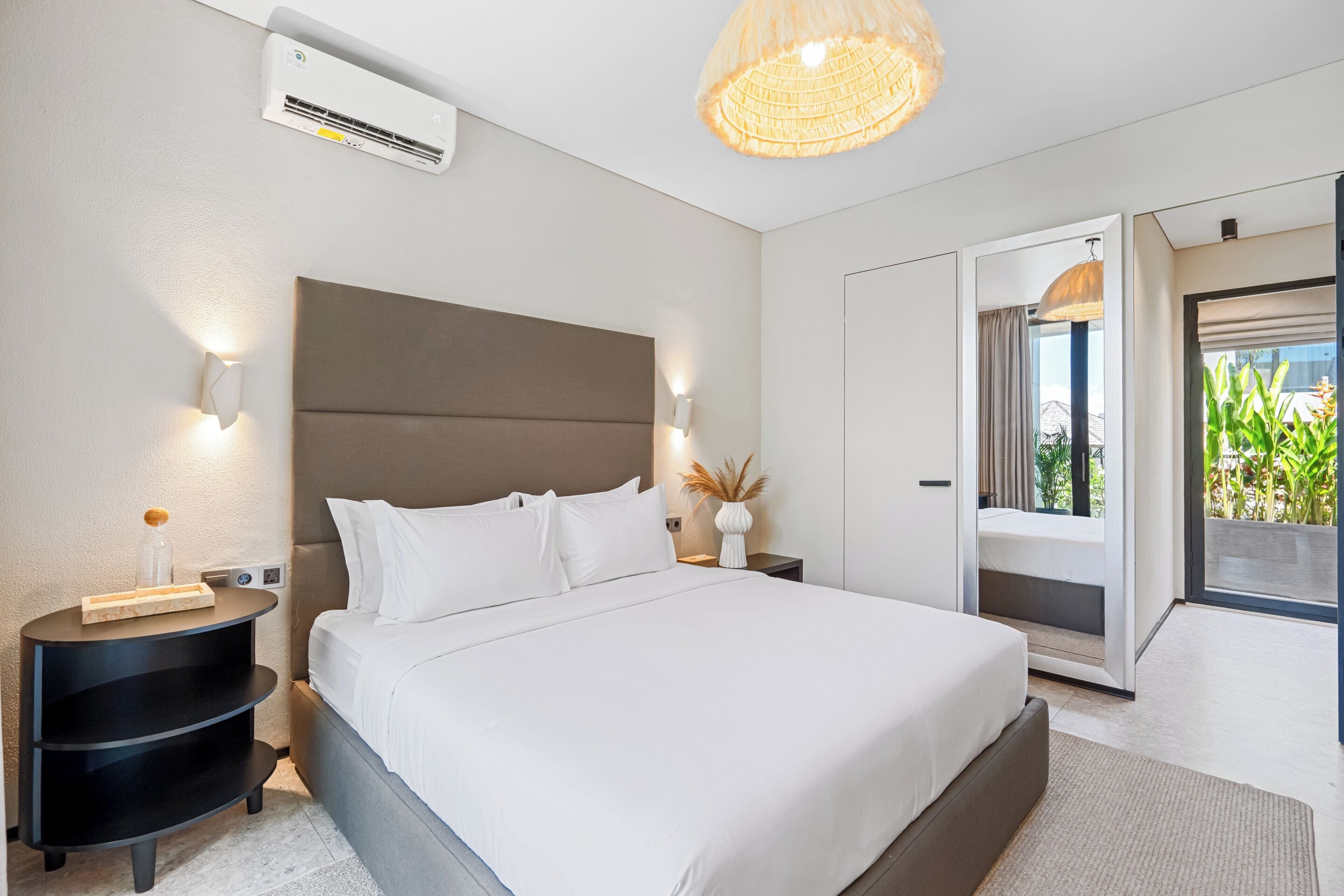 Ein modernes Schlafzimmer mit einem großen Bett, Nachttischen, einer Klimaanlage und Blick ins Freie.