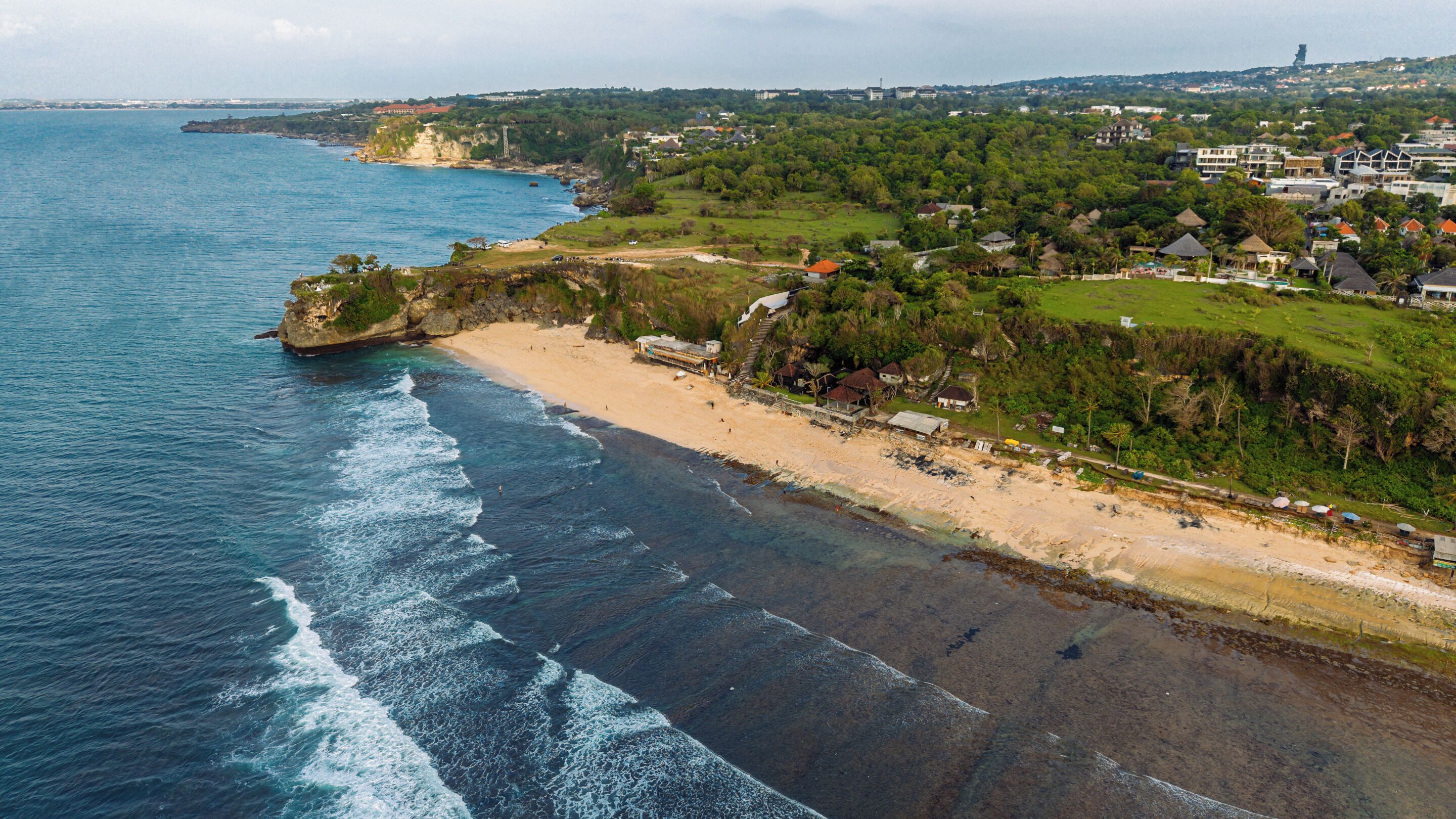 Vista aérea de una zona costera con playa, casas y vegetación.