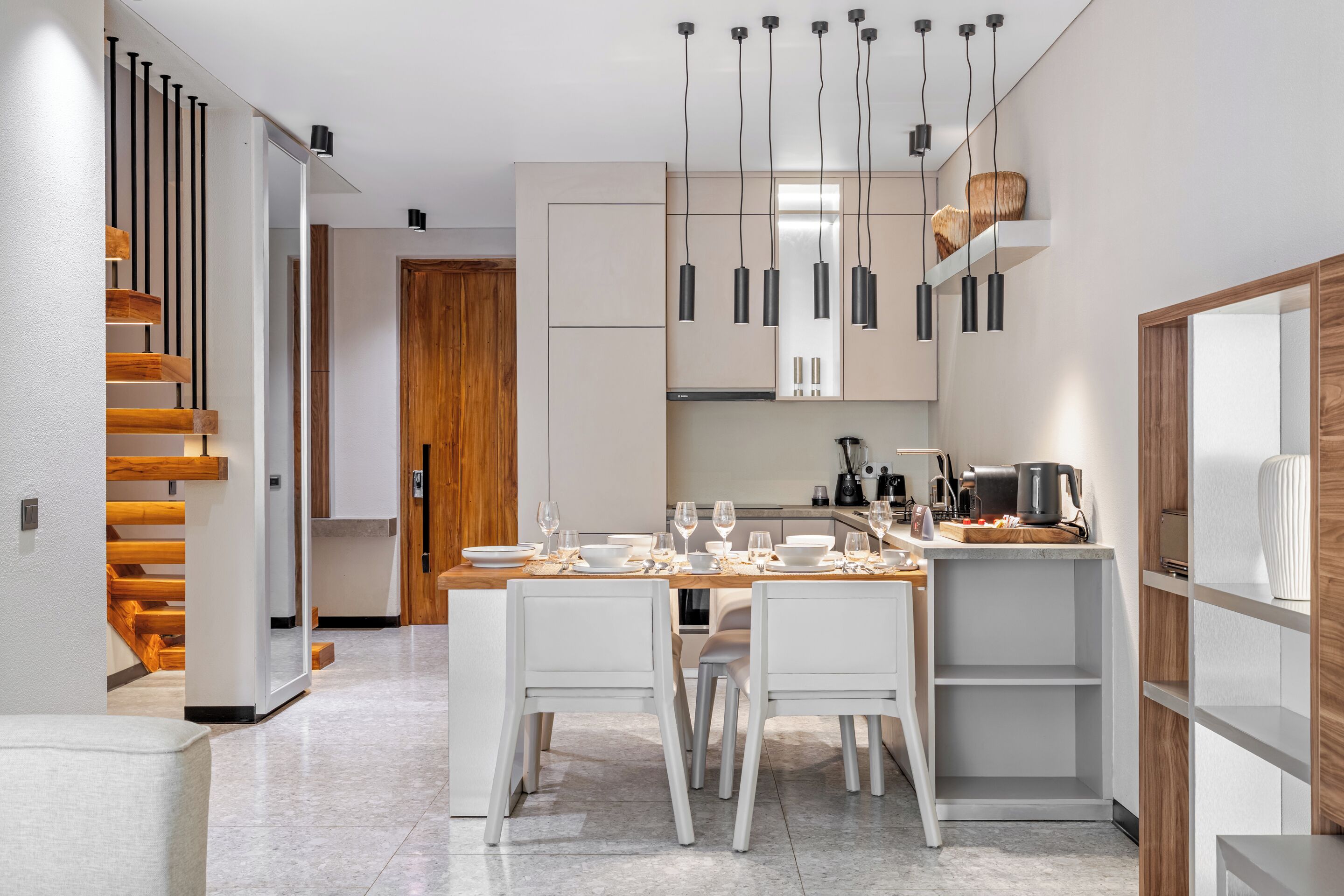 A modern kitchen with white cabinetry, a wooden dining table, and hanging pendant lights.