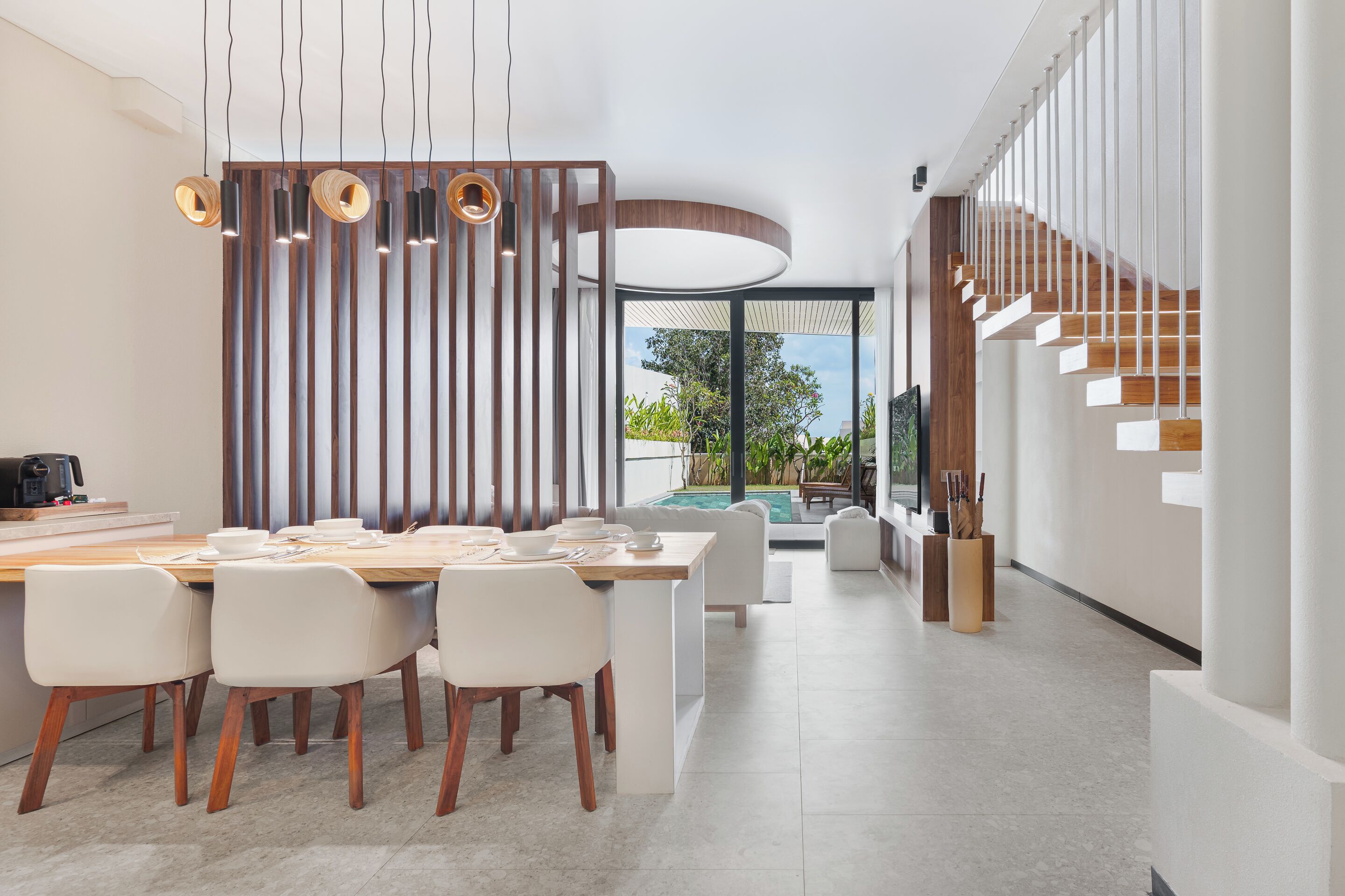 Un comedor moderno con una mesa de madera, sillas blancas e iluminación colgante.