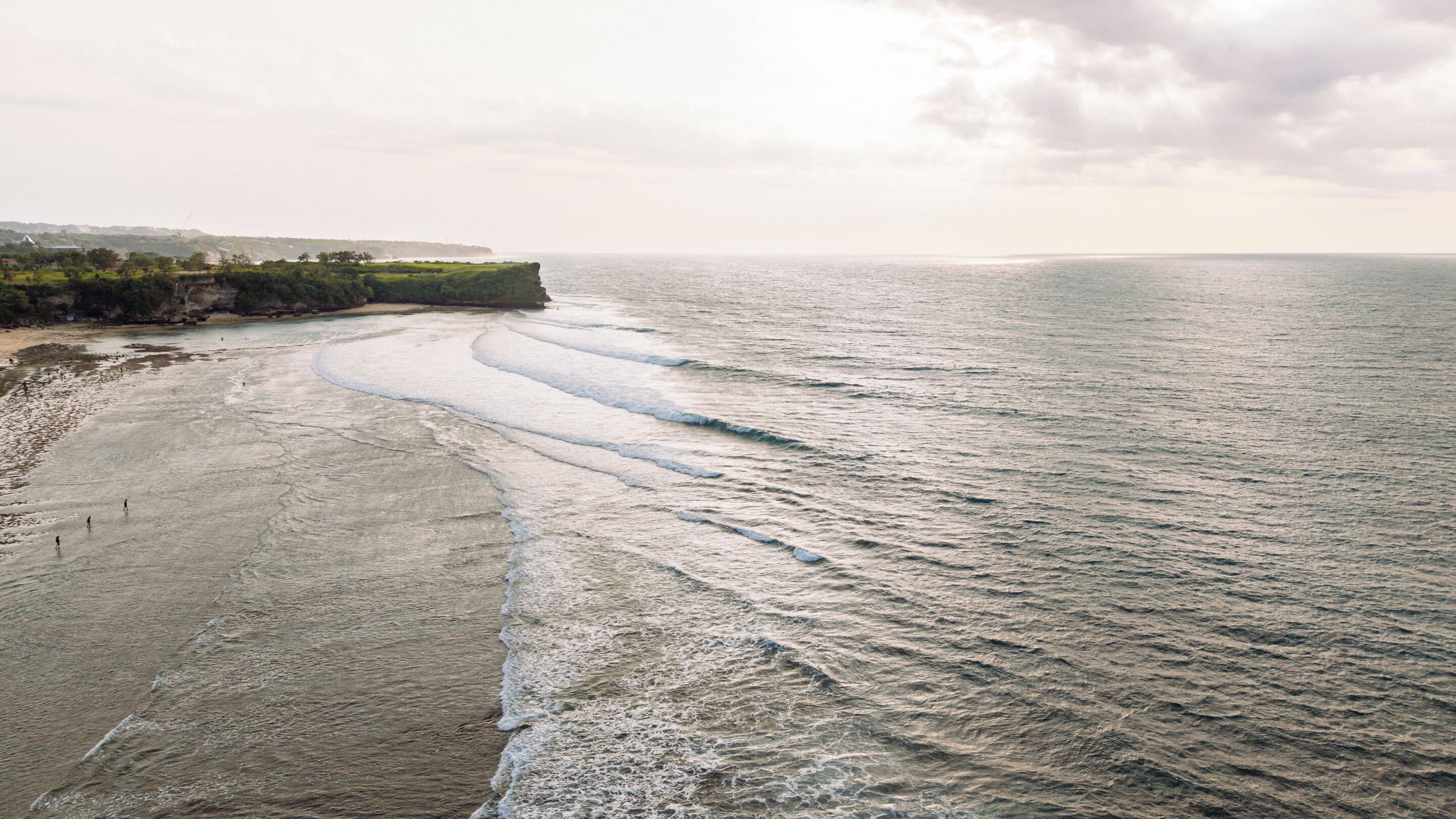 A coastal landscape with a beach, waves, and a distant shoreline.