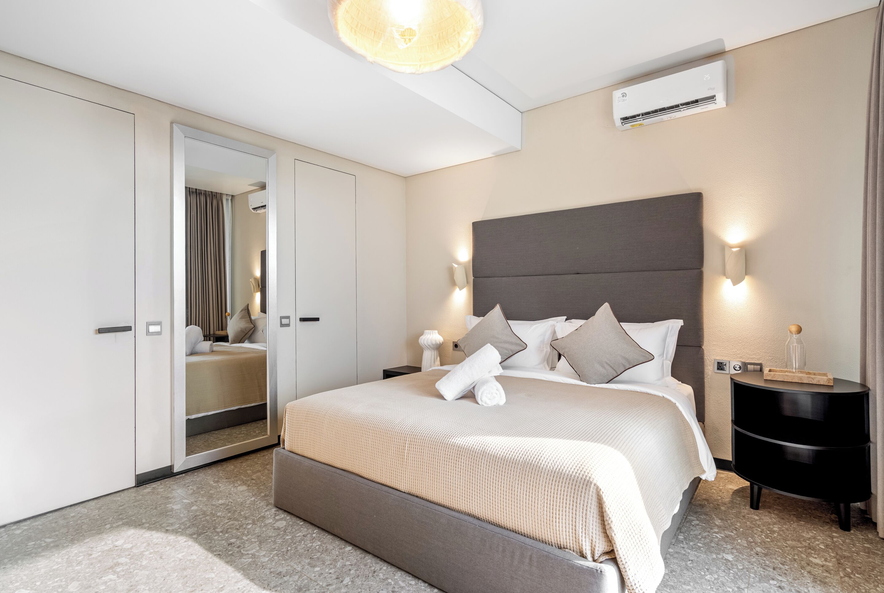 A modern hotel room with a large bed, a wardrobe, a bedside table, and a mirror.