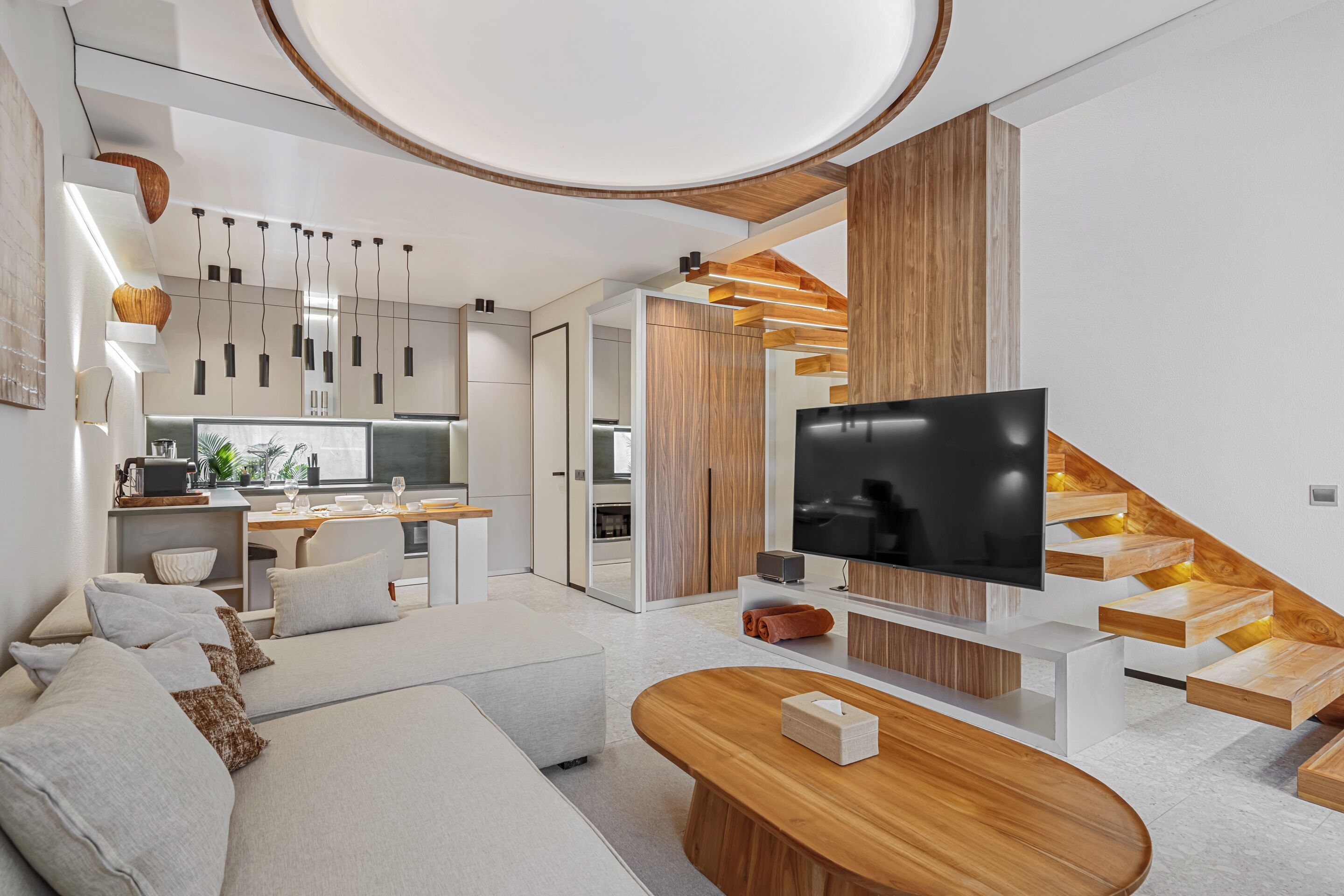 A modern living room with a sofa, coffee table, TV, and wooden staircase.