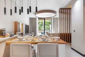 A modern dining area with a wooden table set for six, a large window with a view of greenery, and a contemporary light fixture above. - Balangan Residence (Jimbaran)