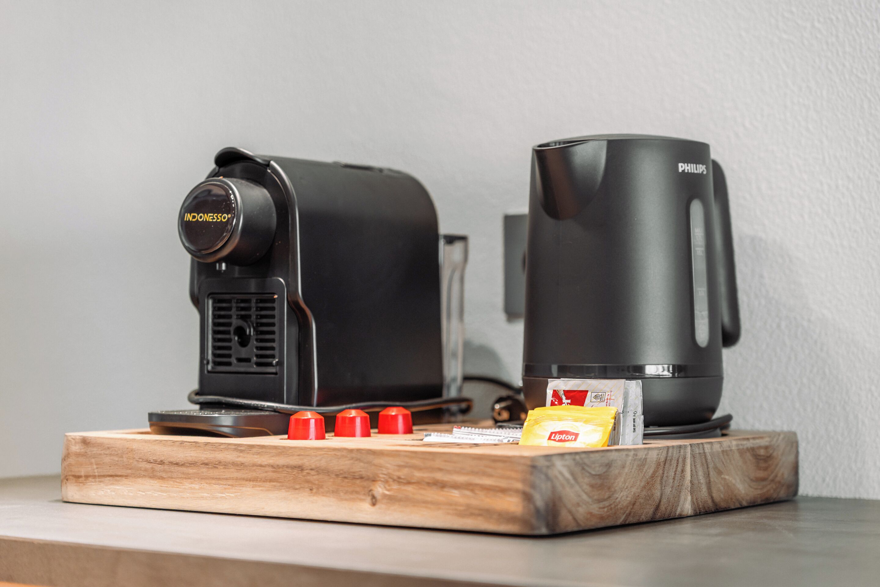 Eine Kaffeemaschine, eine Philips-Kaffeetasse und ein Teebeutel Lipton auf einem Holztablett.