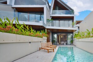 A modern building with a swimming pool, lounge chairs, and a well-maintained garden. - Balangan Residence (Jimbaran)