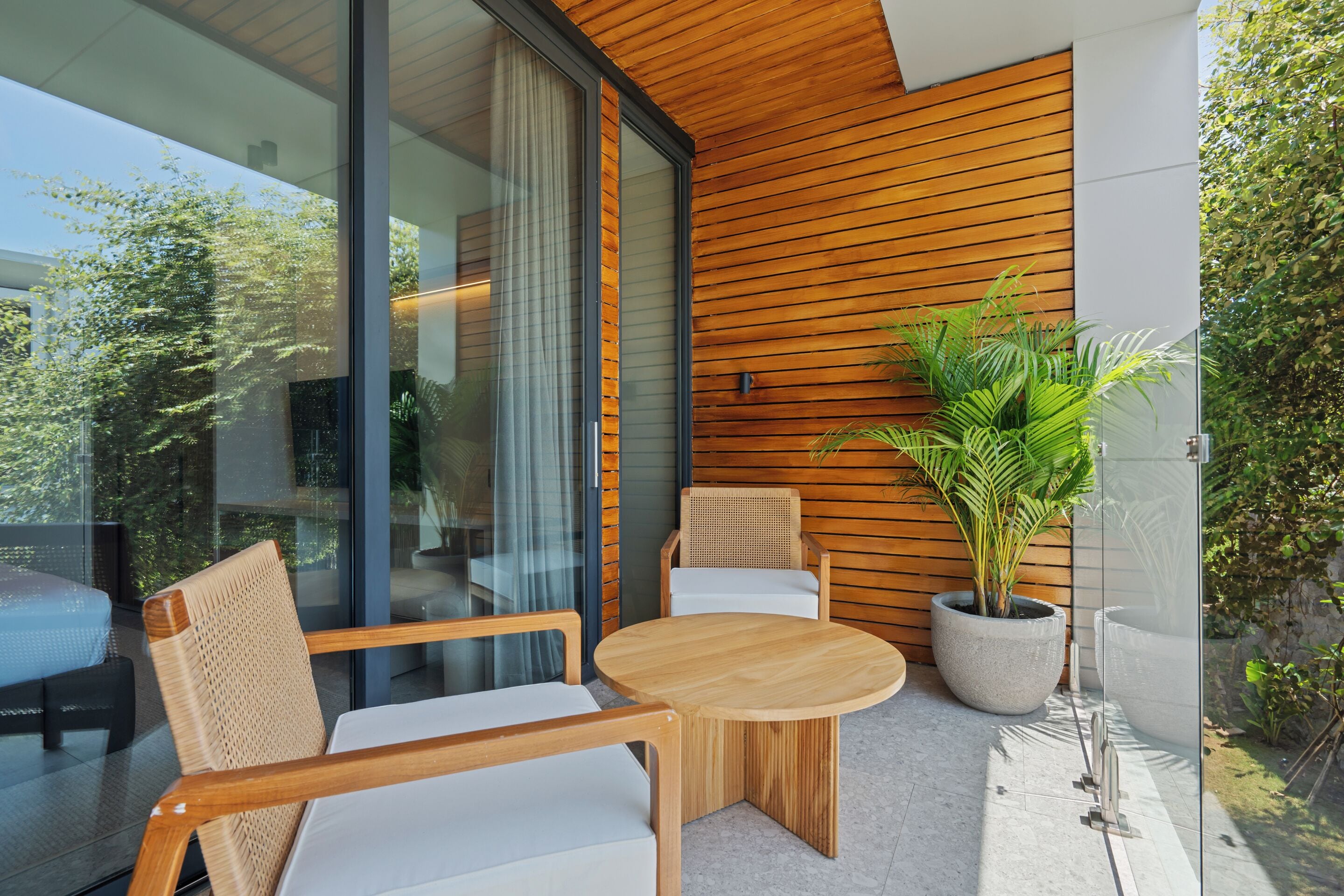 Un espace extérieur moderne aménagé avec du mobilier en bois, une table ronde et une grande plante en pot.