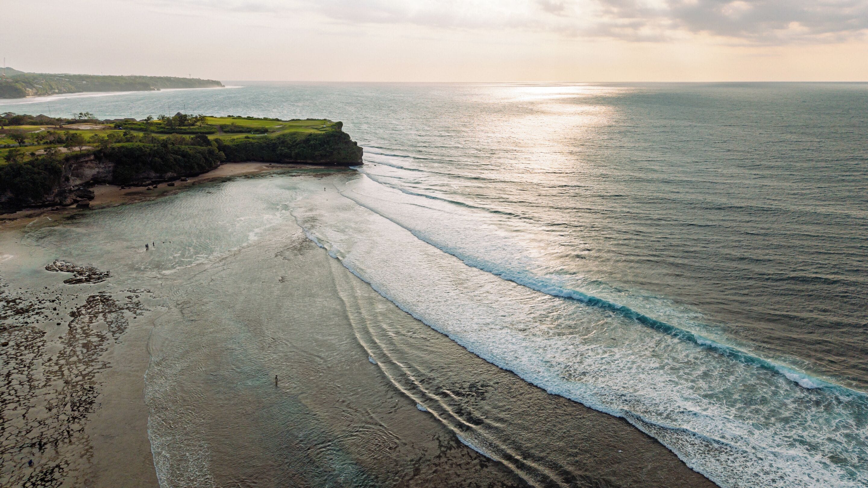 Paisaje costero con playa, océano y tierra en la distancia.