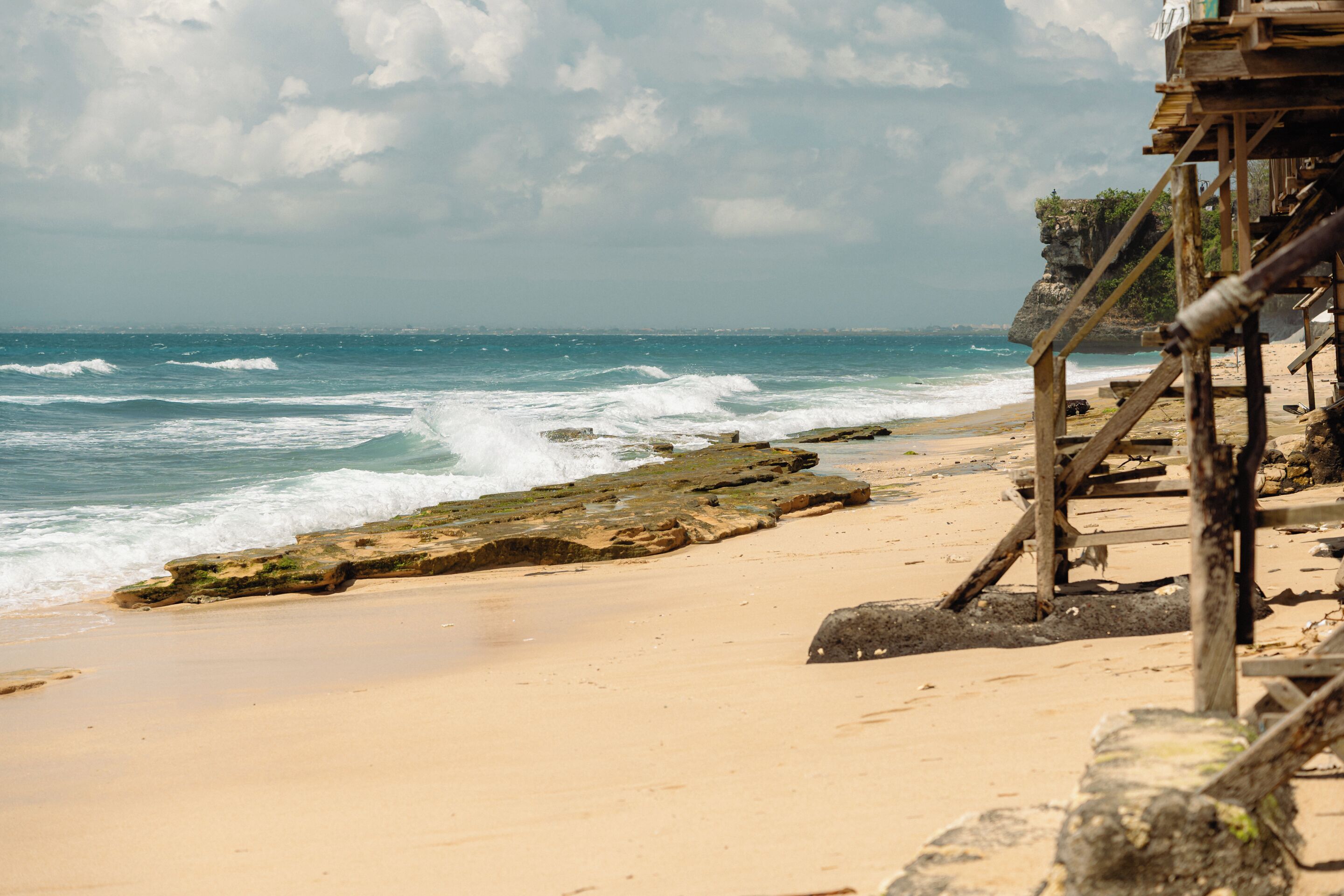 A beach with waves, a wooden structure, and a rocky cliff.