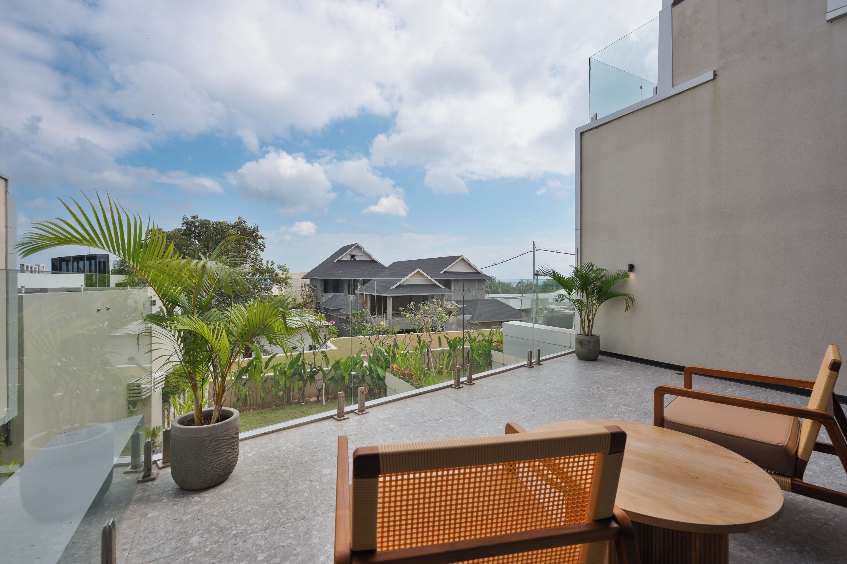 A modern outdoor seating area with a glass balustrade, potted plants, and a view of residential buildings.