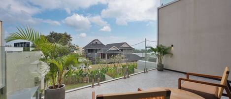 A modern outdoor seating area with a glass balustrade, potted plants, and a view of residential buildings.