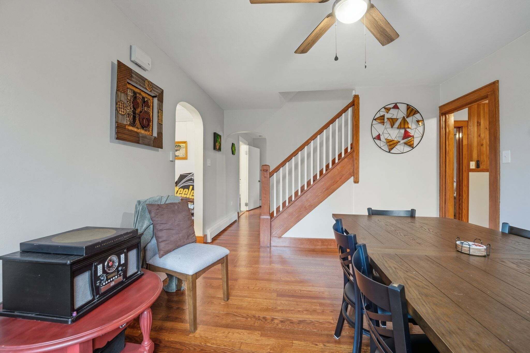 A dining area with a wooden table, chairs, a ceiling fan, and a staircase leading upstairs.