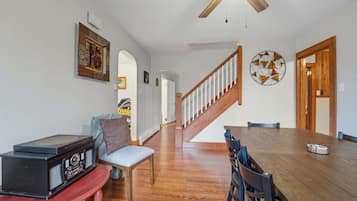 A dining area with a wooden table, chairs, a ceiling fan, and a staircase leading upstairs.