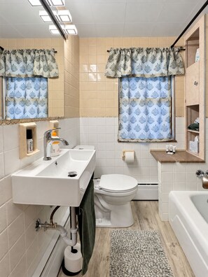 A bathroom with a sink, toilet, and bathtub. There are two windows with patterned curtains. - Johnstown Stay Near Laurel Highlands & Hiking (Johnstown)
