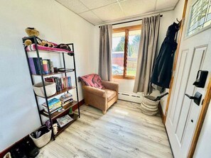 Una habitación pequeña con estantería, una silla, ventana con cortinas y una puerta.