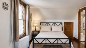 A bedroom with a bed, bedside table, lamp, radiator, and a window with curtains. - Johnstown Stay Near Laurel Highlands & Hiking (Johnstown)