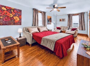 A bedroom with a bed, a sofa, a wooden floor, a ceiling fan, and artwork on the walls. - Johnstown Stay Near Laurel Highlands & Hiking (Johnstown)