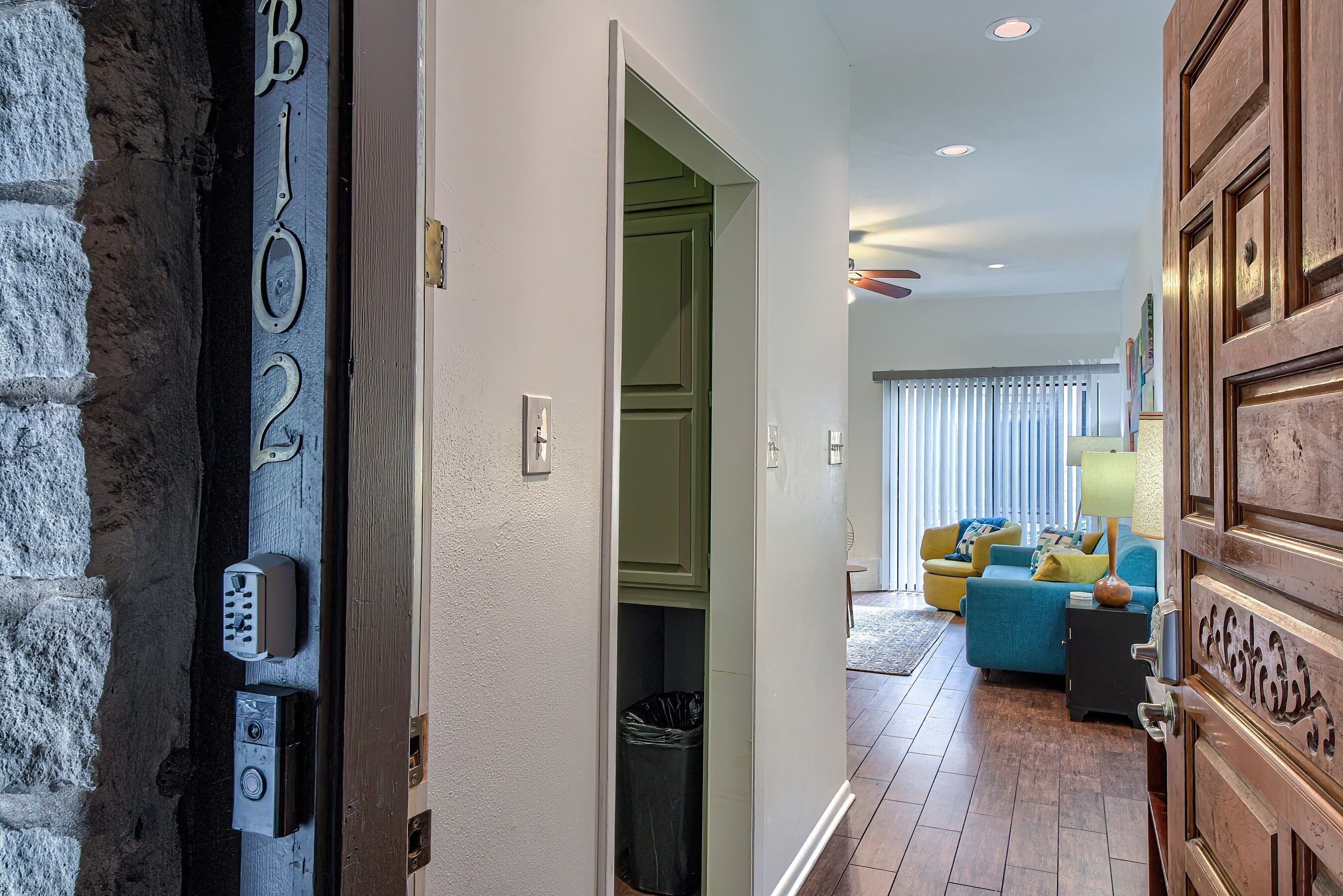 Een gang met een deur waarop 'B102' staat en een moderne woonkamer met een bank en lamp.