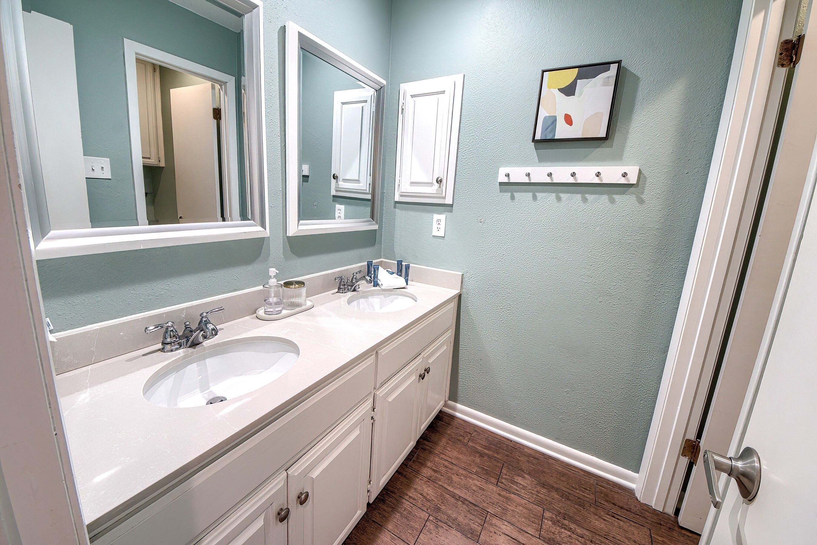 A bathroom with two sinks, a large mirror, and a door with a handle.