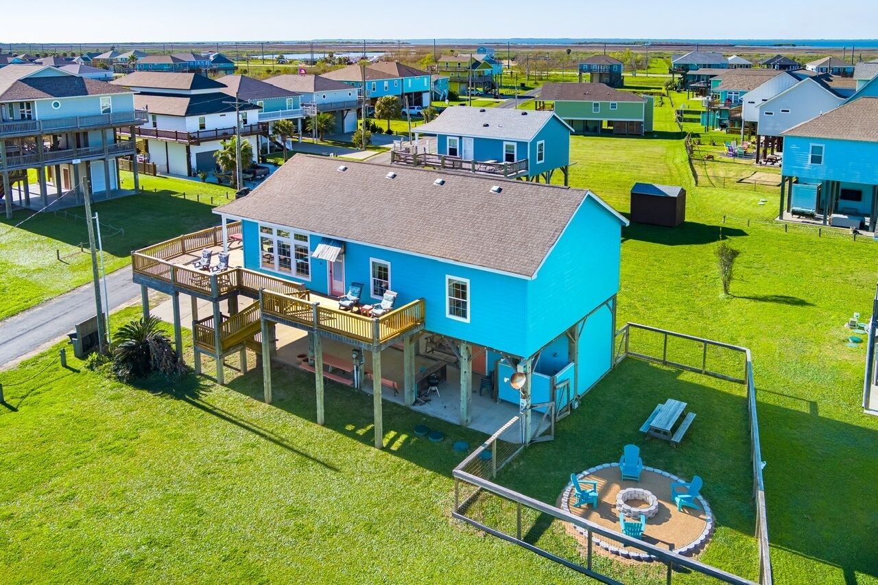 Un quartier résidentiel avec des maisons, dont une grande maison bleue dotée d’une terrasse et d’une cour clôturée.
